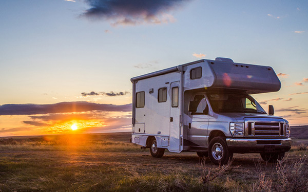 Image of an RV in the middle of a grass field at sunset.