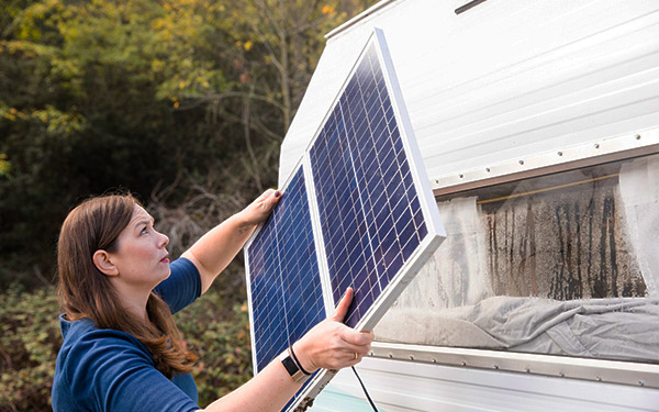 Image shows a person installing a solar panel to their RV.