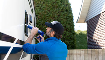 person applying a sealant to the outside rv window to prevent water damage