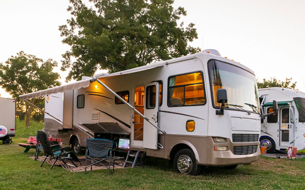 Image of an RV and different RV accessories at an RV park. RV is parked with extended shade cover.