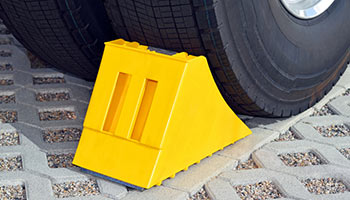 Image of an rv accessory. Shows a wheel chock wedged between a wheel. 