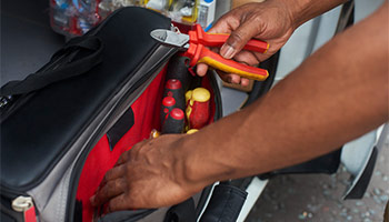 Image of an individual reaching into a tool bag and taking out a set of pliers. 