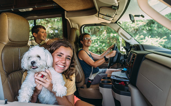 Image shows a family inside of an RV. One child is holding a white colored dog and smiling.