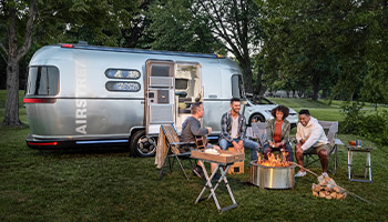 Image shows a group of friends sitting outside an eStream, which is an eco friendly trailer made by Airstream and Thor Industries. 