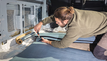 a person adding insulation to their RV like you would to insulate your RV during winter. Person is applying fabric insulation to the floor. 
