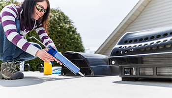 A women applying caulk to the outside of her RV like you would to insulate your RV. She is wearing a striped shirt that is purple and white. 