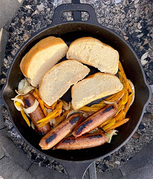 brats, bell peppers, onions and bread in a cast iron pan 
