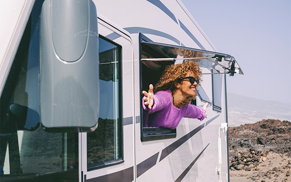 a person standing outside of an RV window smiling with sunglasses on