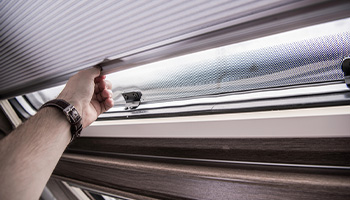 person pulling down an RV window cover to help RV stay cool