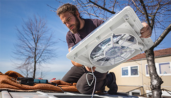 person installing an RV vent cover with a fan at the top of their RV