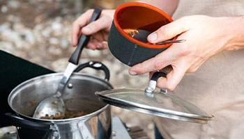 A person serving themselves food from a camp cooking pot