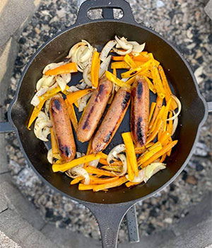 grilled bratwurst, onions, and peppers in a cast iron pan
